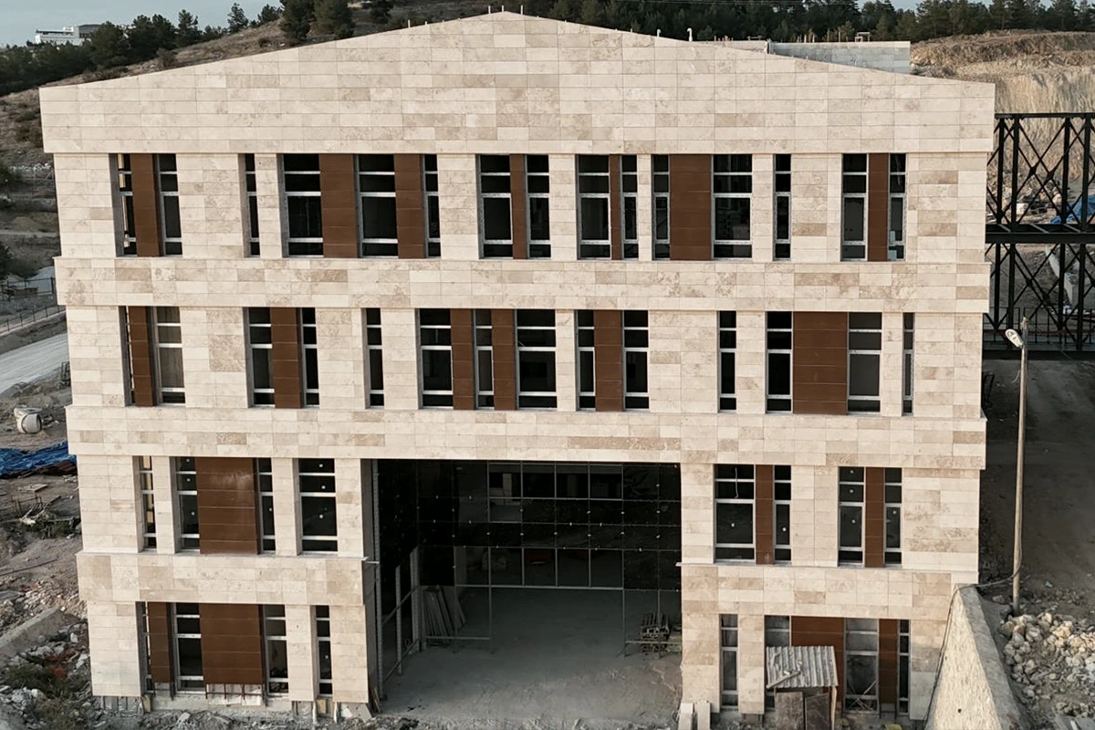 Merkezi Derslik binasının taş kaplı ön cephesi, kahverengi panel dolgular ve pencere ızgarası.
